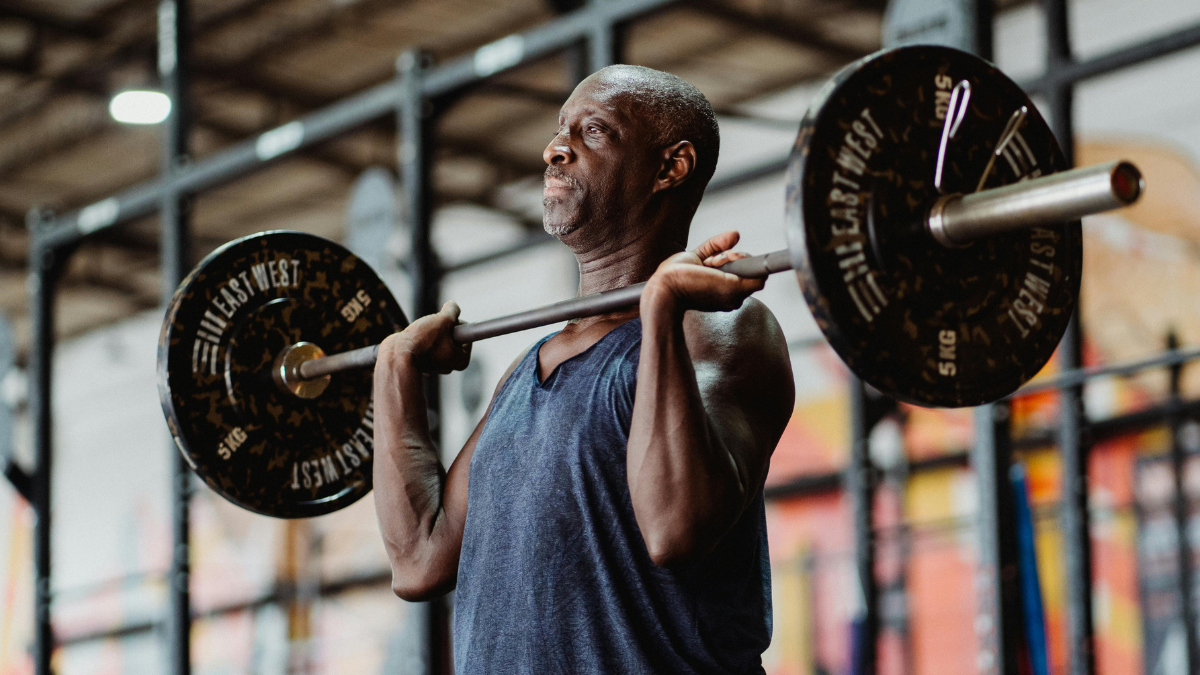 Older man lifting a heavy barbell in the front rack position at the gym