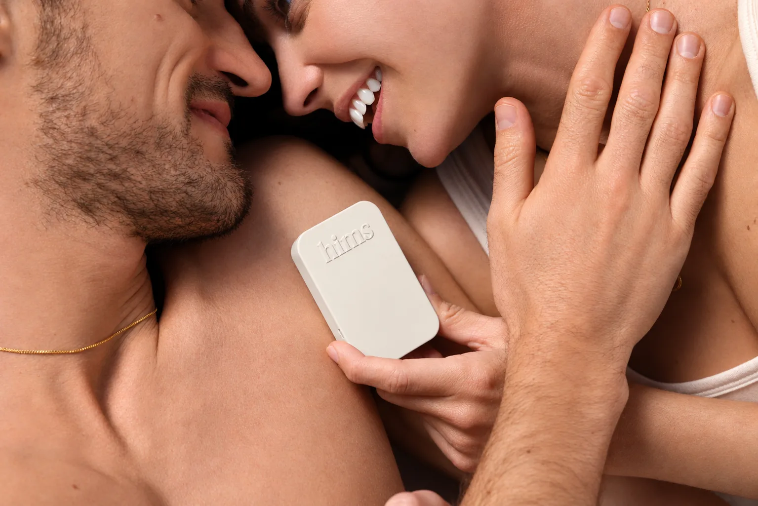 A male and female couple in bed holding a tin of Hims ED plan