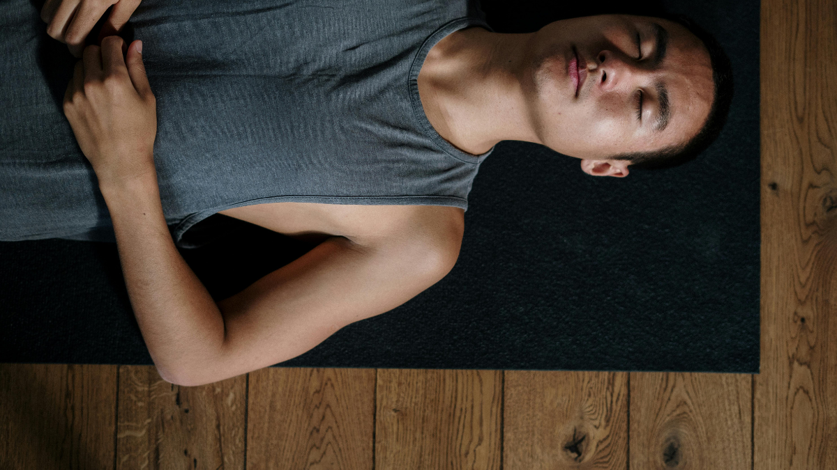 Man lying on a yoga mat with eyes closed practicing relaxation to manage stress