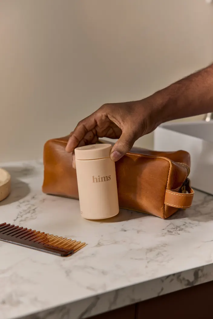 A product image of a hand holding a hims bottle
