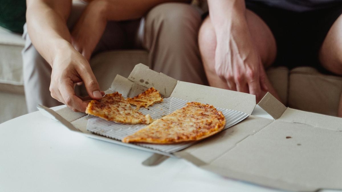 Man reaching for leftover pizza from a takeaway box late at night on the couch