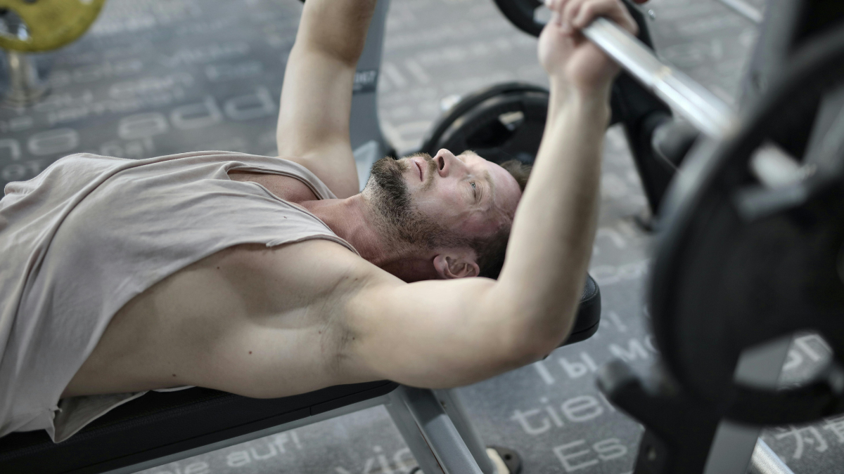 Man bench pressing a barbell at the gym, using progressive overload to build muscle