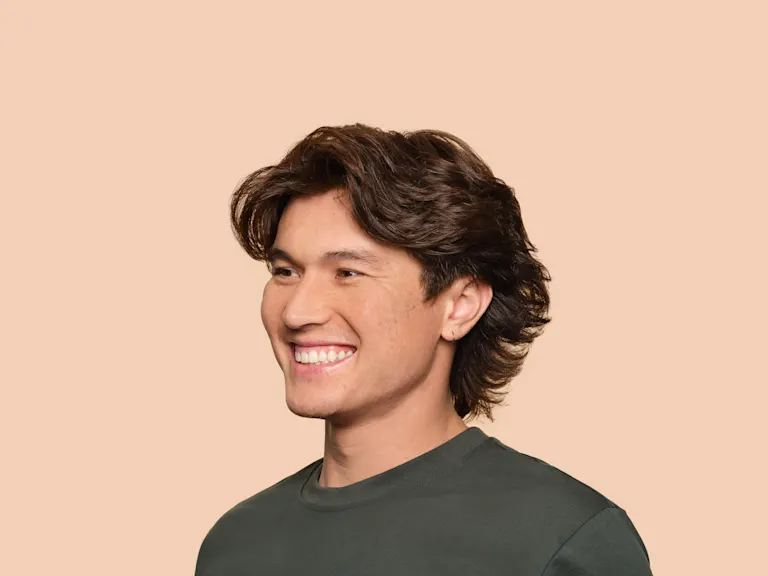 A young man looks excitedly off camera with a studio wall behind him