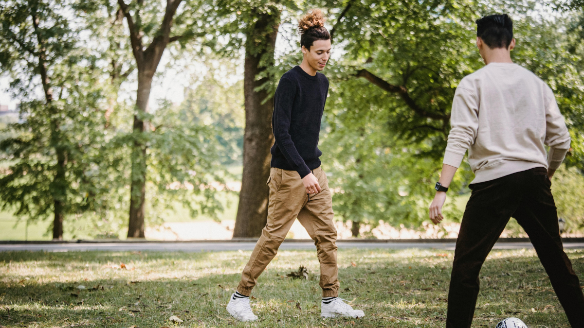 Two men kicking a football in a park, regular exercise that supports healthy testosterone