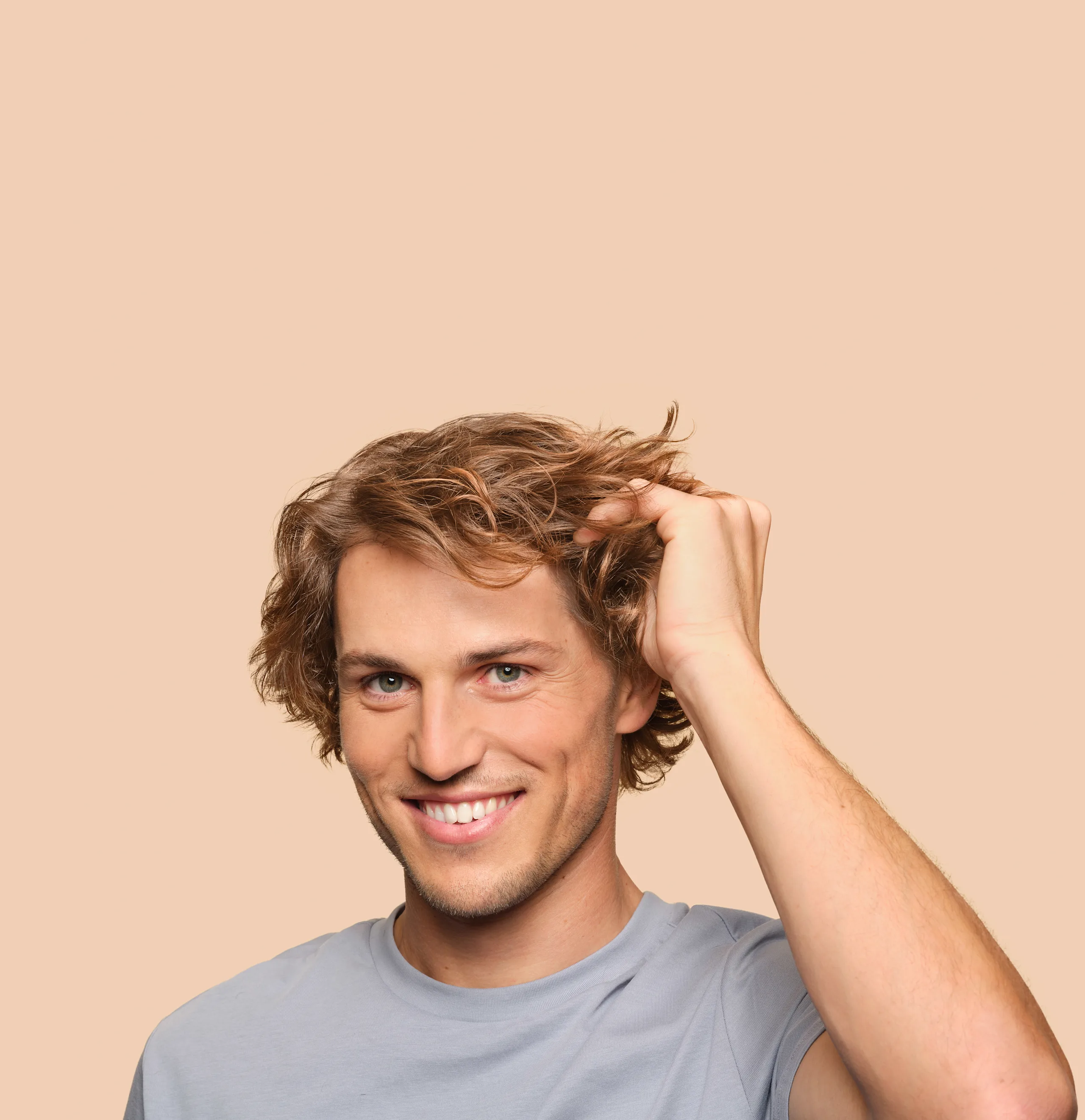Young man smiles at camera and plays with his hair