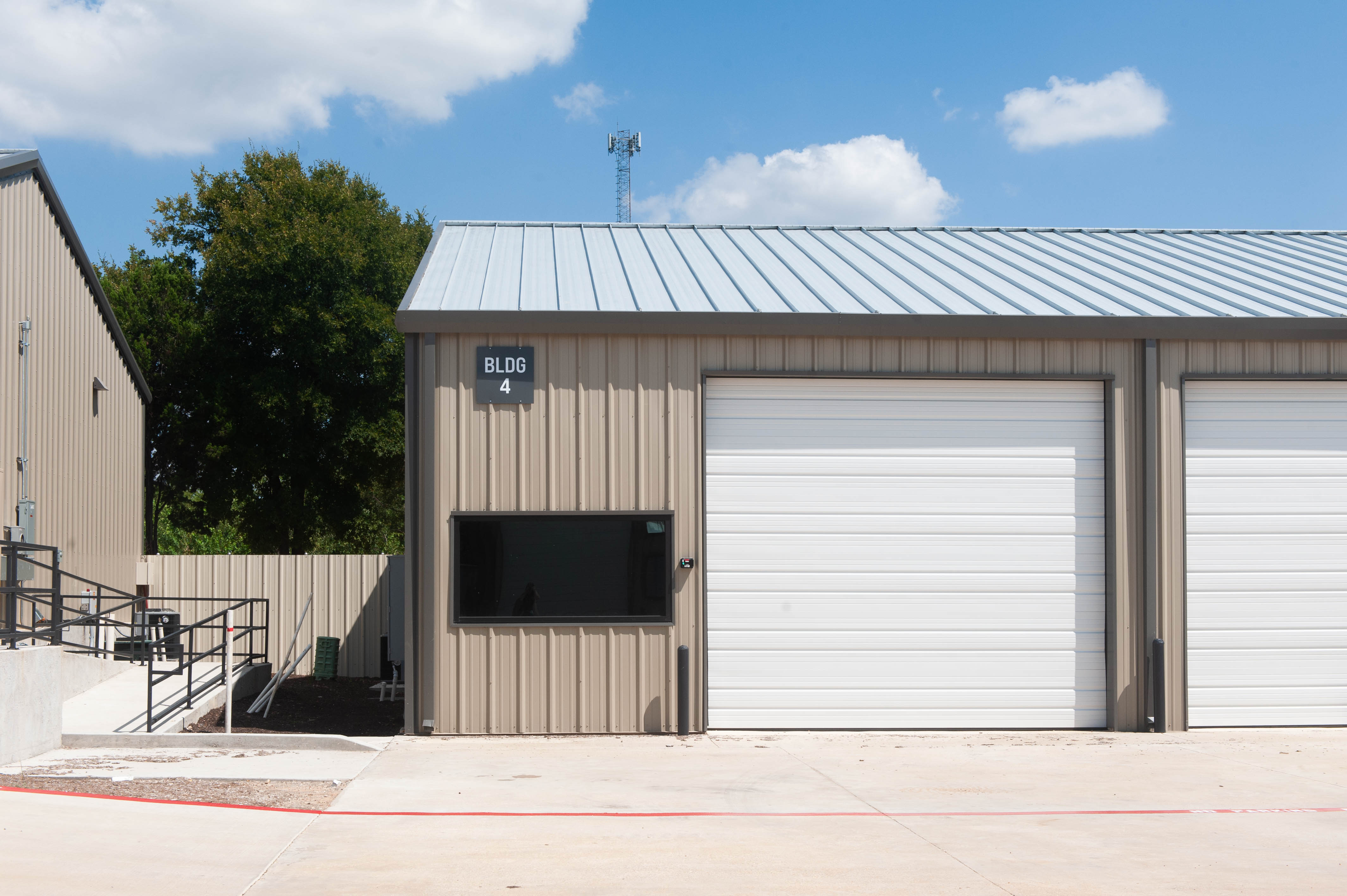 Frontal view of brown metal industrial one-story building with bldg 4 logo and white garage and a metal roof