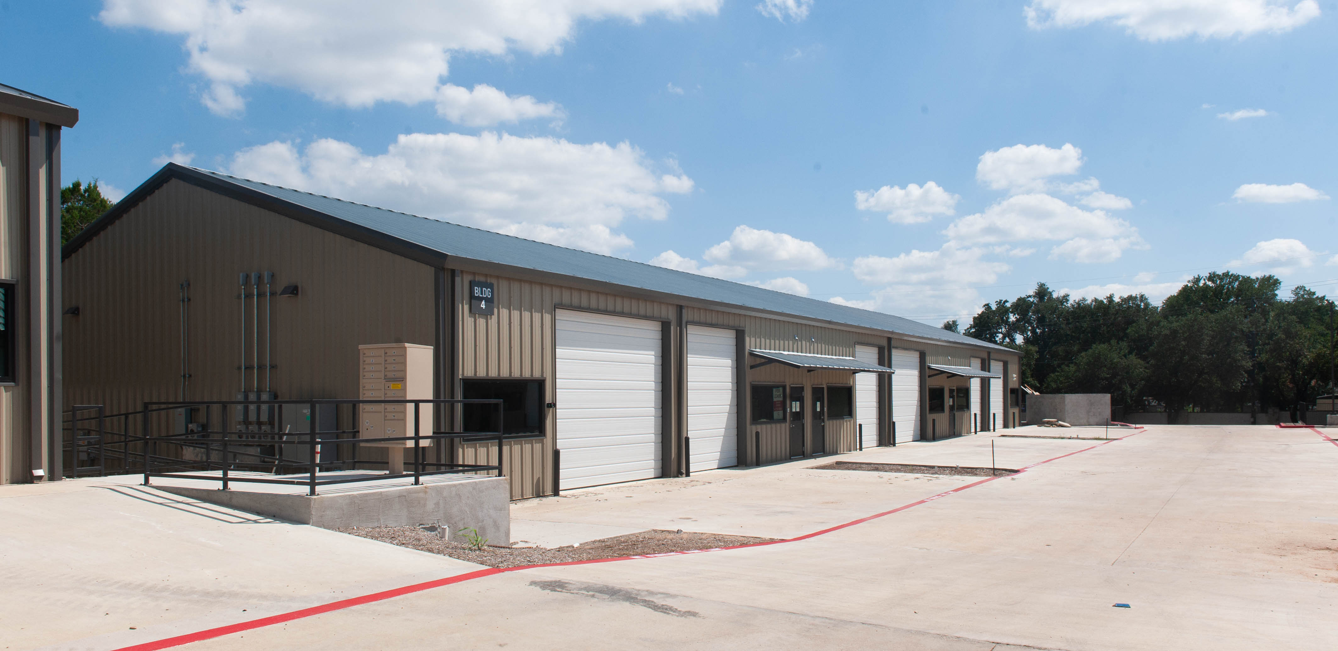 Image of a metal industrial warehouse painted brown with gray roof and white garage doors with concrete loading docks in the front