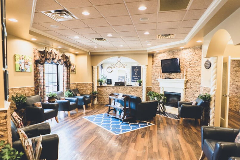 The interior of the dentist's office has a wood floor, black leather chairs, a TV, and a stone wall mixed with beige-painted walls.