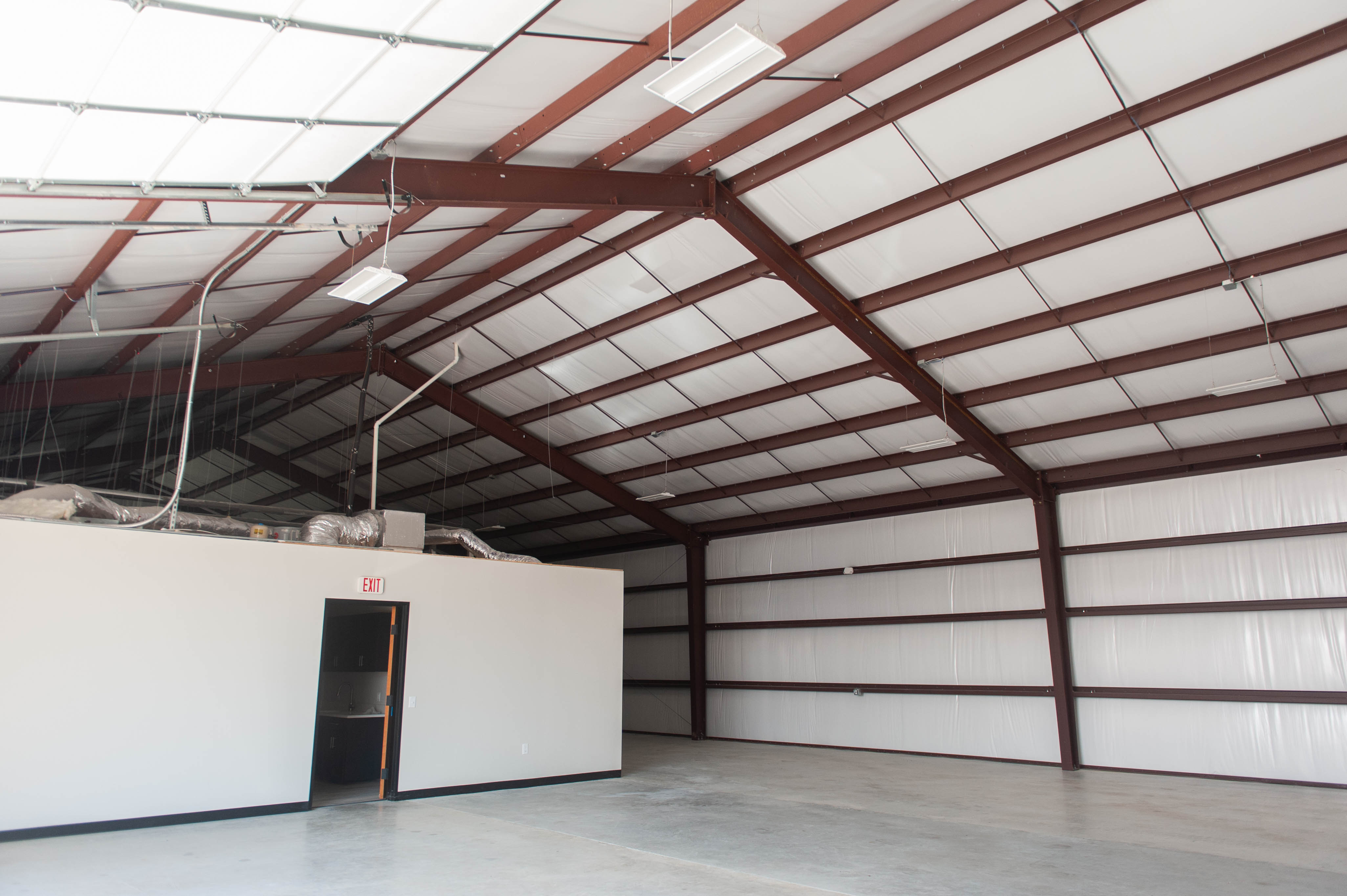 Inside of empty industrial building with concrete floor and center office space with HVAC piping and insulated walls