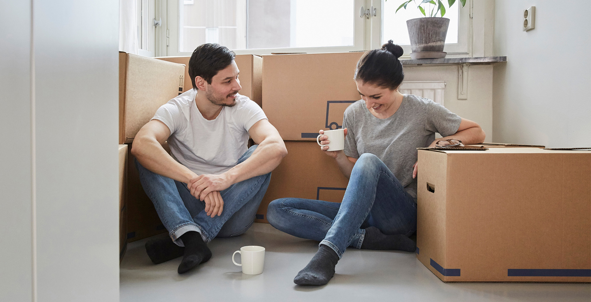 En kvinna och en man sitter och dricker kaffe bland flyttkartonger.