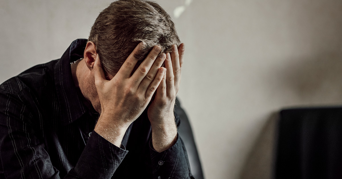 En kille sitter med händerna framför ansiktet.