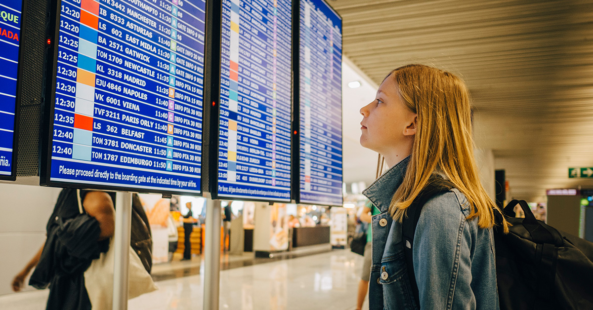 Tjej står och tittat på avgångstavla på flygplats.