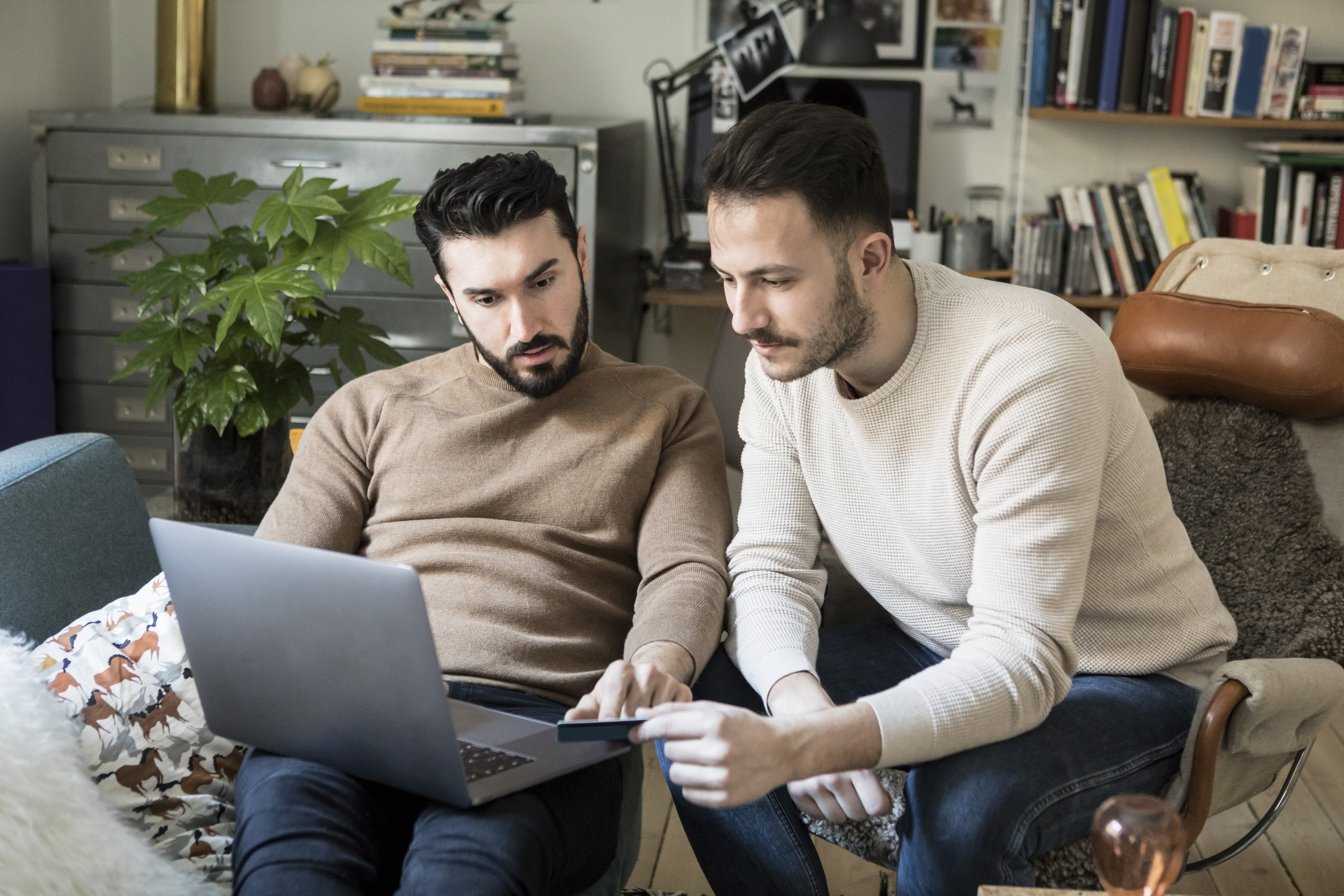 Två män sitter framför en laptop. En har ett betalkort i handen.