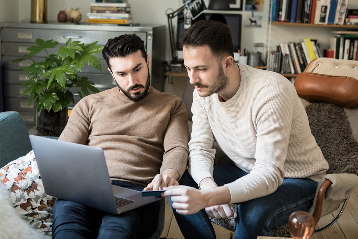 Två män sitter framför en laptop. En har ett betalkort i handen.