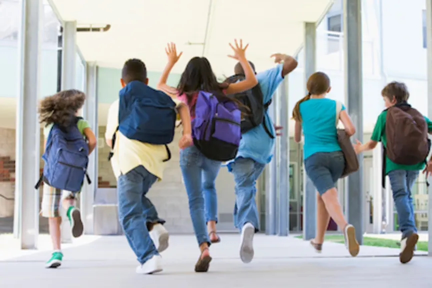 Children running into school with backpacks on.