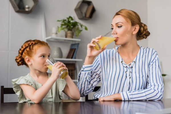 母亲和女儿在喝橙汁。