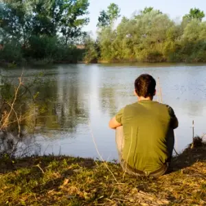一个男人坐着，看着一个湖