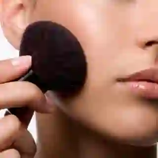 Women applying makeup to cheek with brush.