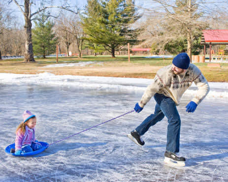 男人穿着冰鞋拉着小女孩的雪橇。