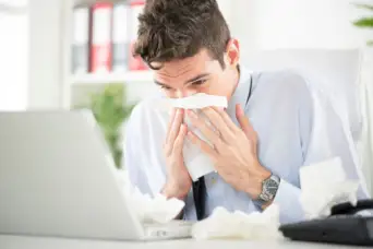 一个男人在工作中生病，吹他的鼻子在他的桌子上。
