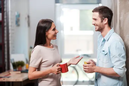 佩带浅色的t恤的妇女微笑和谈话与一个人。两者都拿着咖啡杯。