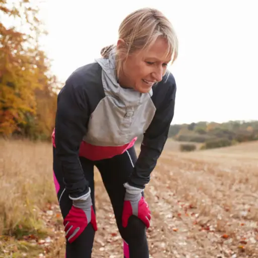 Mature Female Runner Pausing For Breath During Exercise In Woods