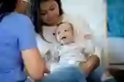 Baby smiles while being examined by a nurse or doctor during a house call medical exam.