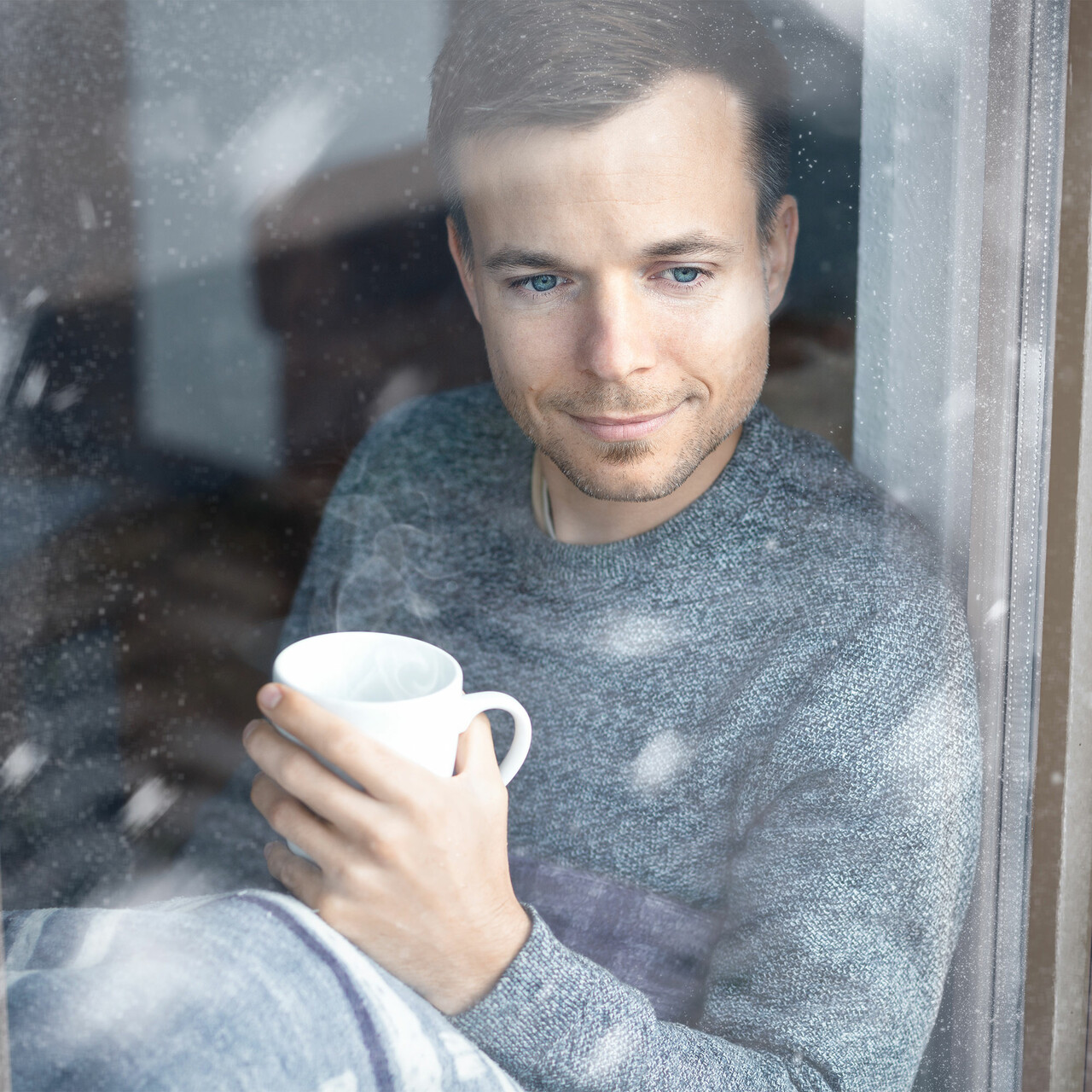 一个男人拿着杯子看起来的一个窗口在一个下雪的天