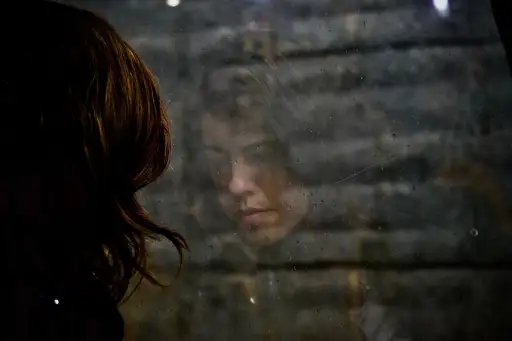 一个悲伤的女人从后面望向窗外，反射着脸