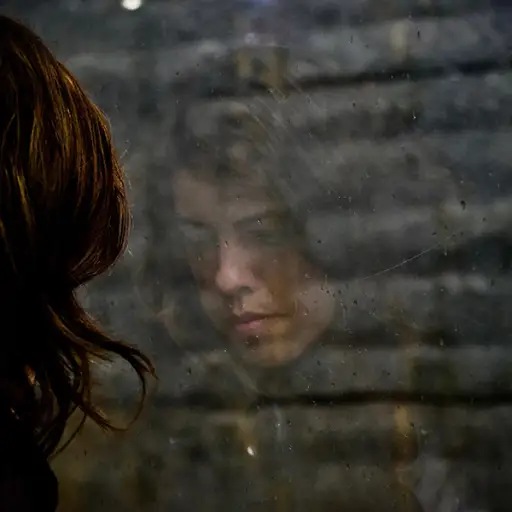 一个悲伤的女人从后面看着窗户，脸上的倒影