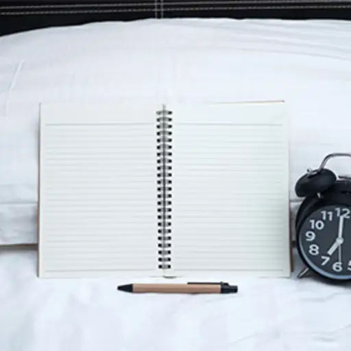 Sleep journal, pen, alarm clock on bed.