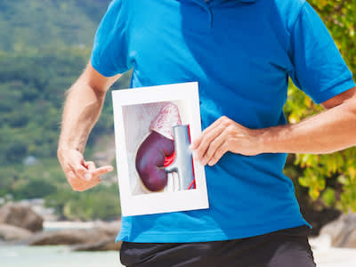 一个男人拿着肾的图片在身体的实际肾位置前。