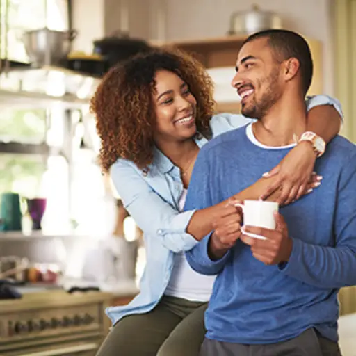 Couple hugging while drinking coffee in the kitchen.