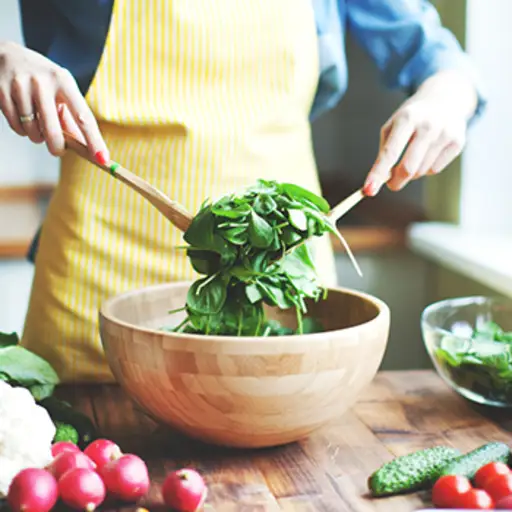 Woman mixing salad in wooden bowl.