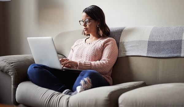 一名年轻女子坐在家里的沙发上进行网上研究。