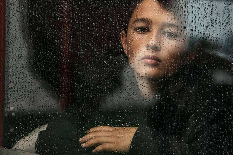 悲伤的小男孩透过雨中的窗户。