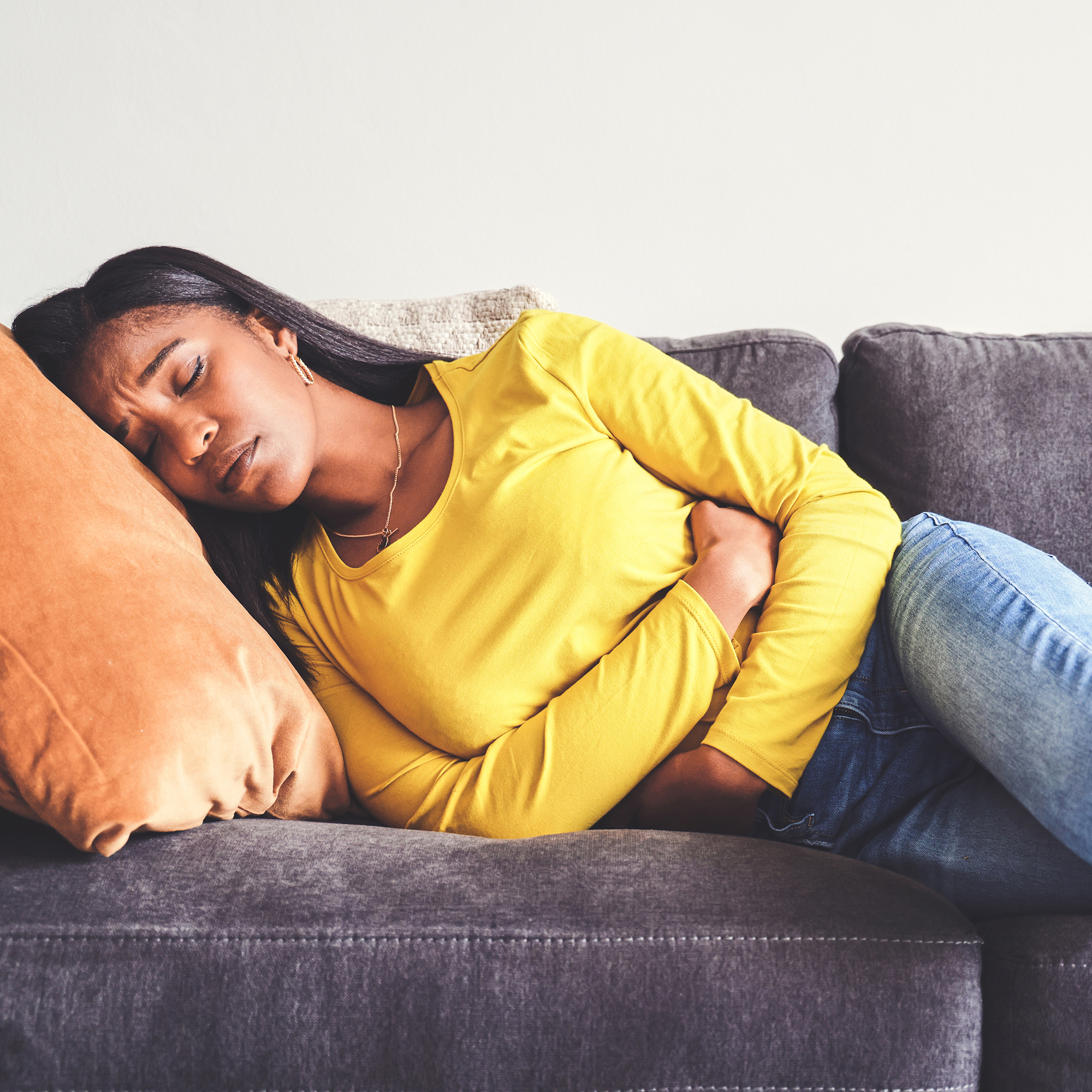 一名妇女躺在家里的沙发上感到胃痛