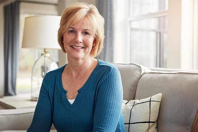 年长的成年妇女微笑地坐在家里的沙发上。