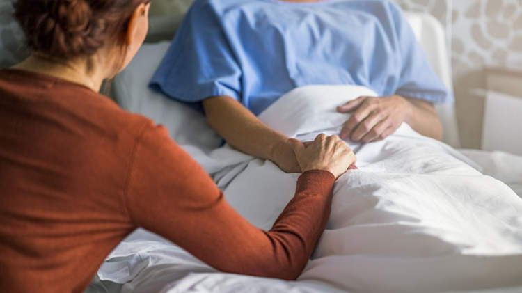 妇女牵着手在医院的病床上。