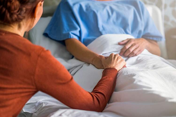 妇女牵着手在医院的病床上。