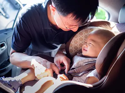 把婴孩放的微笑的父亲在汽车座位。