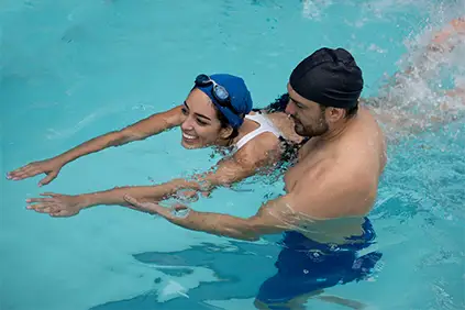 微笑的女子在男教练的指导下上游泳课。