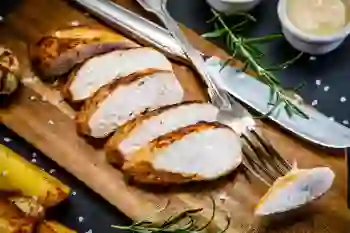 Sliced grilled chicken breast with cutlery on a cutting board.