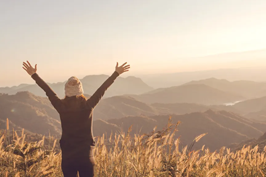 一名女子在空中举起双臂，俯瞰着山景。