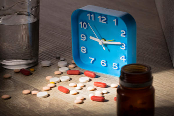 安眠药,闹钟,药瓶,并在床头柜上的一杯水。