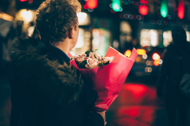 晚上，一名男子手持鲜花站在城市的街道上