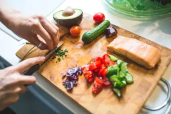woman chopping chives, preparing meal of salmon and vegetables on cutting board