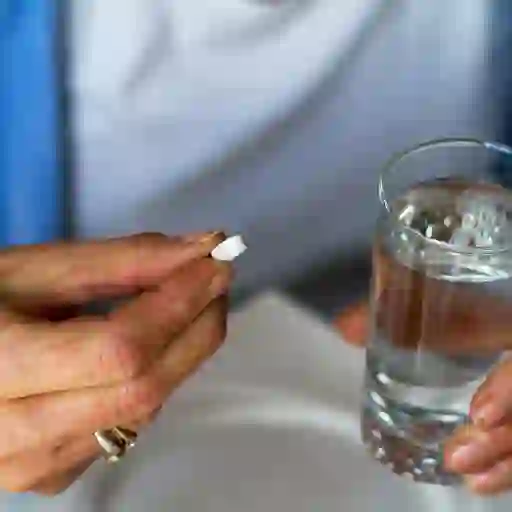 一个人拿着一颗药丸和一杯水的画面
