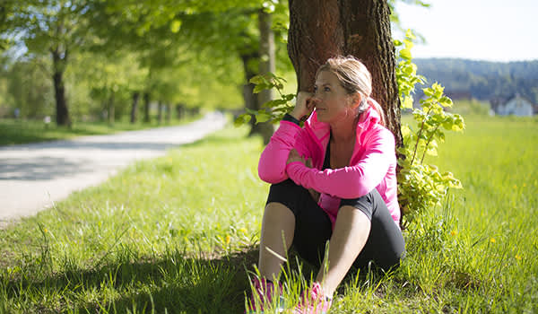 女人采取中止锻炼时间由靠在一棵树