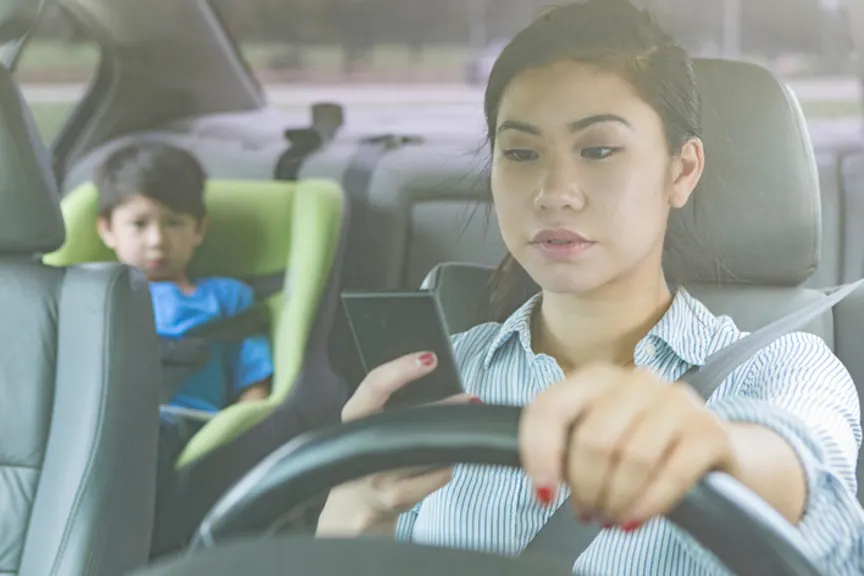 Mother driving and using cell phone while child is in back seat.